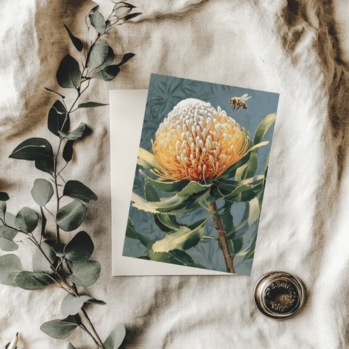 A 5x7 folded greeting card displaying an intricate watercolor illustration of an Australian native golden Banksia cone with a small honeybee flying above it. The left panel features a textured cream background with a gold ink Willow and Wag Australia logo.