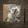 A 5x7 folded greeting card featuring a detailed watercolor painting of a fluffy koala sitting in a white gum tree surrounded by green eucalyptus leaves and white blossoms. The left panel shows a textured off-white finish with the gold ink Willow and Wag Australia logo.