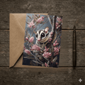 A 5x7 folded greeting card featuring a moody watercolor painting of a cute sugar glider clinging to a branch surrounded by pink grevillea blossoms. The artwork transitions smoothly to a textured charcoal back panel featuring the gold ink Willow and Wag Australia logo.