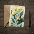 A 5x7 folded greeting card featuring a detailed watercolor illustration of golden Australian native Wattle blossoms with dark green leaves and a small native bird perched on a branch. The left panel shows a textured off-white finish with the Willow and Wag Australia logo printed in gold ink.