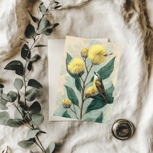 A 5x7 folded greeting card featuring a detailed watercolor illustration of golden Australian native Wattle blossoms with dark green leaves and a small native bird perched on a branch. The left panel shows a textured off-white finish with the Willow and Wag Australia logo printed in gold ink.